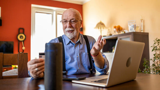 Man with laptop out talking to an artificial intelligence home-assistance device.