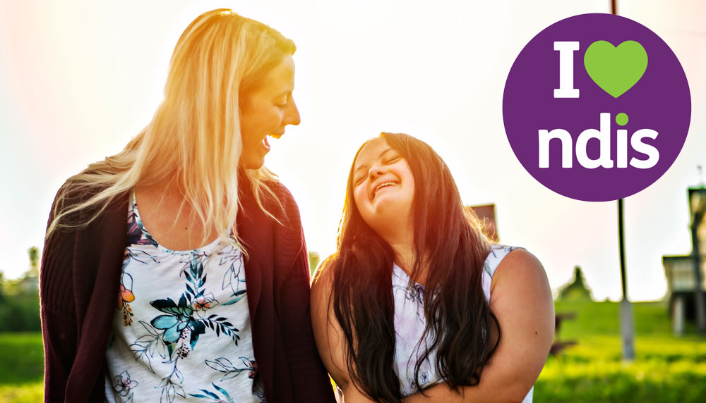 support worker and person smiling at each other in the sun with the NDIS logo to the top right corner of image.